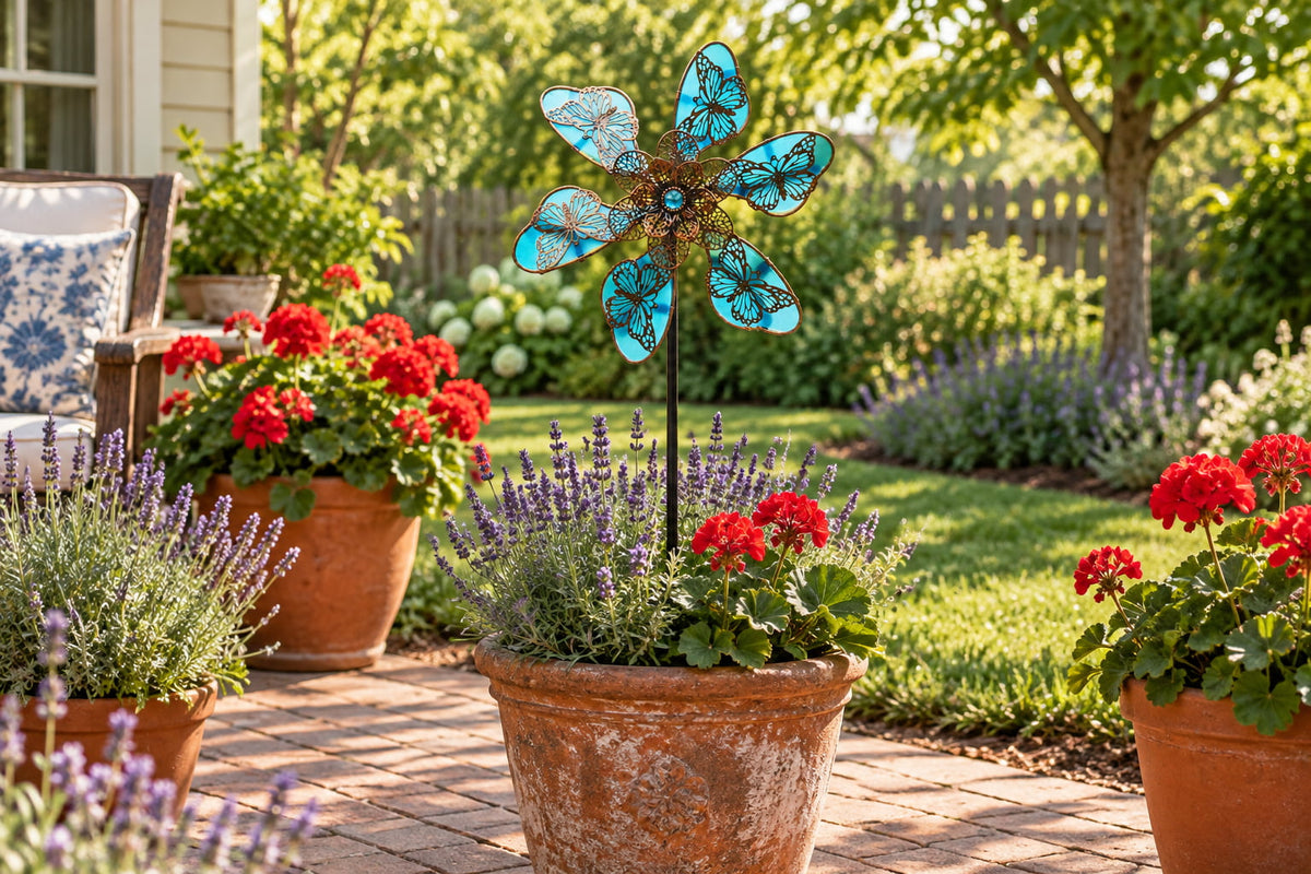 Kinetic butterfly wind spinner staked in a terracotta garden planter surrounded by potted geraniums and lavender on a patio