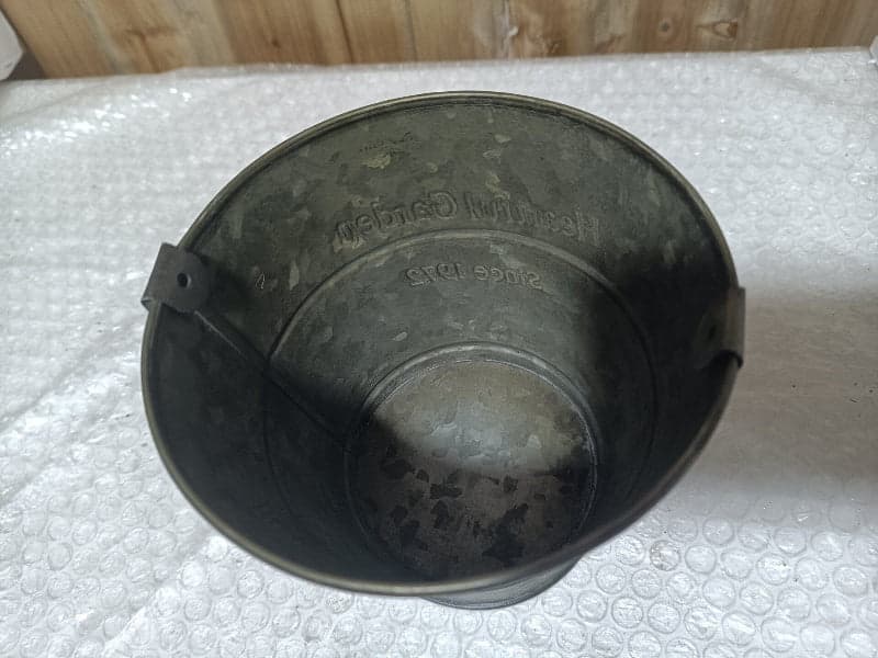 Metal planter bucket top view, embossed text on open rim and side tabs.
