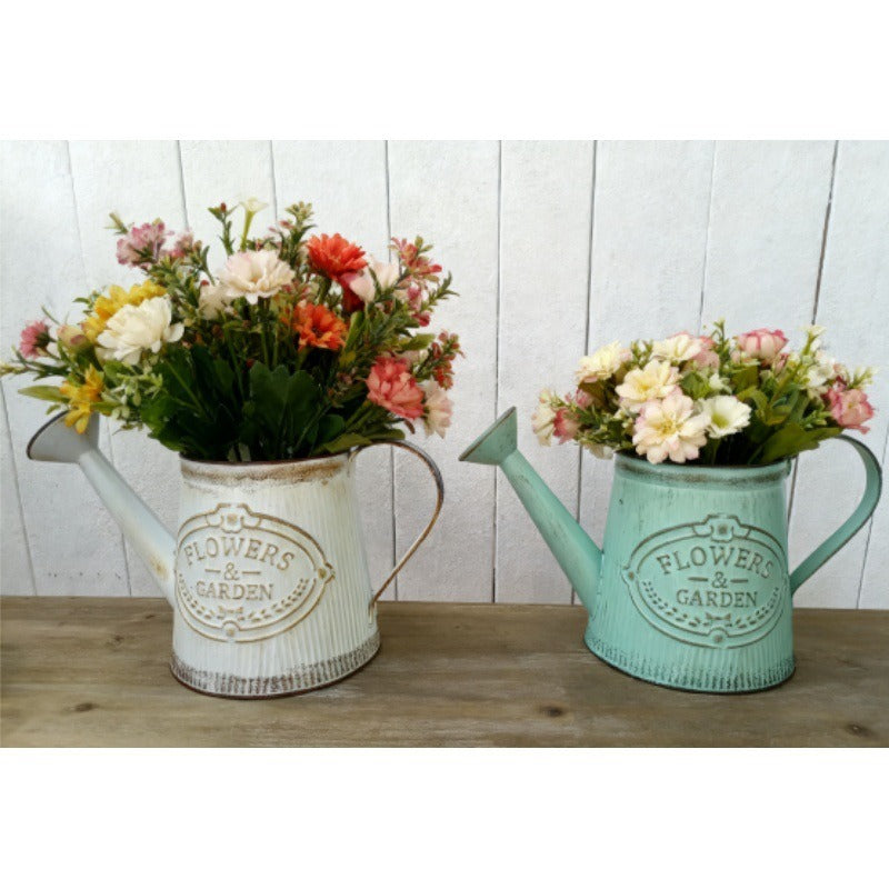 White and teal metal watering can vases with 'Flowers & Garden' emblem, filled with flower bouquets.