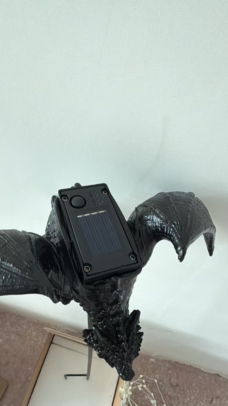 Lámpara de estaca con forma de dragón negro, panel solar visible y guirnalda de luces de luz cálida.