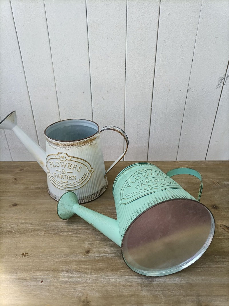 Teal and white metal watering can vase set with 'Flowers & Garden' emblem, spout and lid visible.