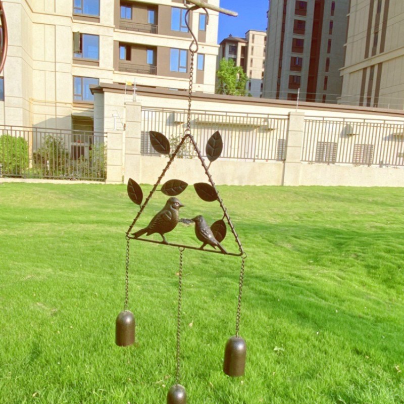 Campana de viento triangular de bronce con recortes de pájaros y dos badajos colgantes.
