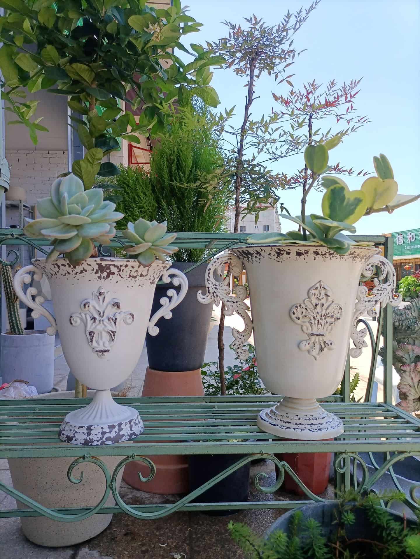 Decorative planters with ornate designs on a metal stand outdoors.