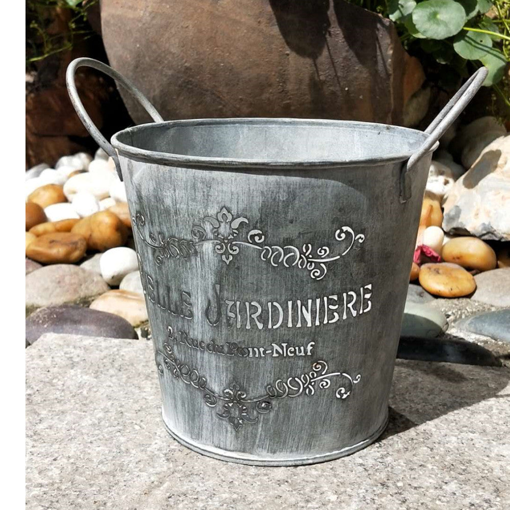 Metal garden bucket with decorative text on a stone surface