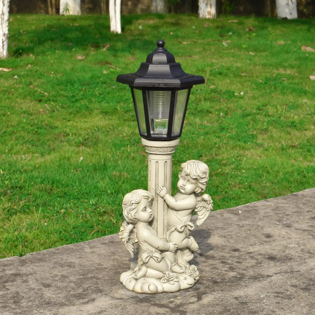Decorative outdoor lamp with angel figures on a stone ledge against a grassy background