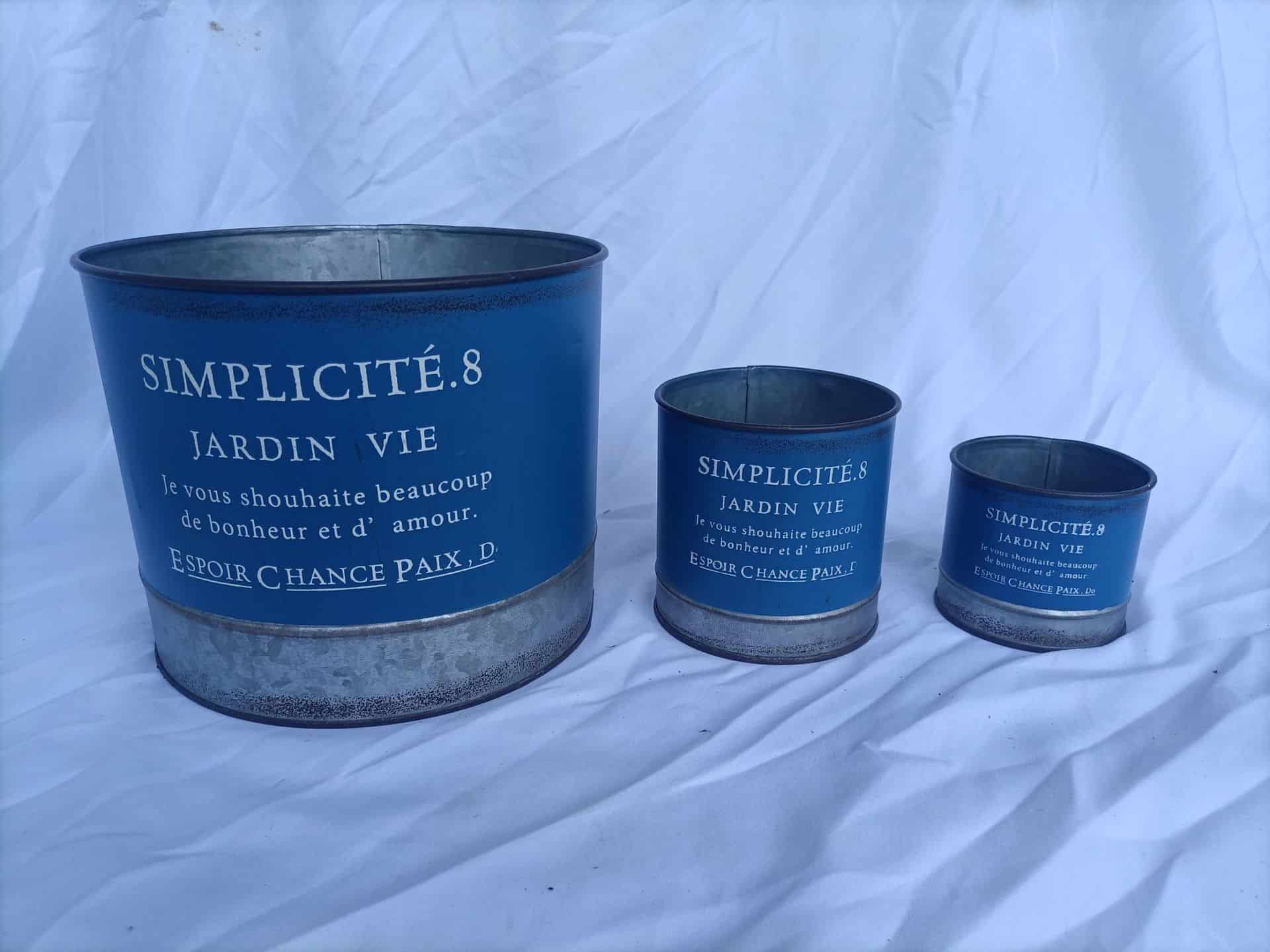 Three blue metal planters with French text on a white fabric background