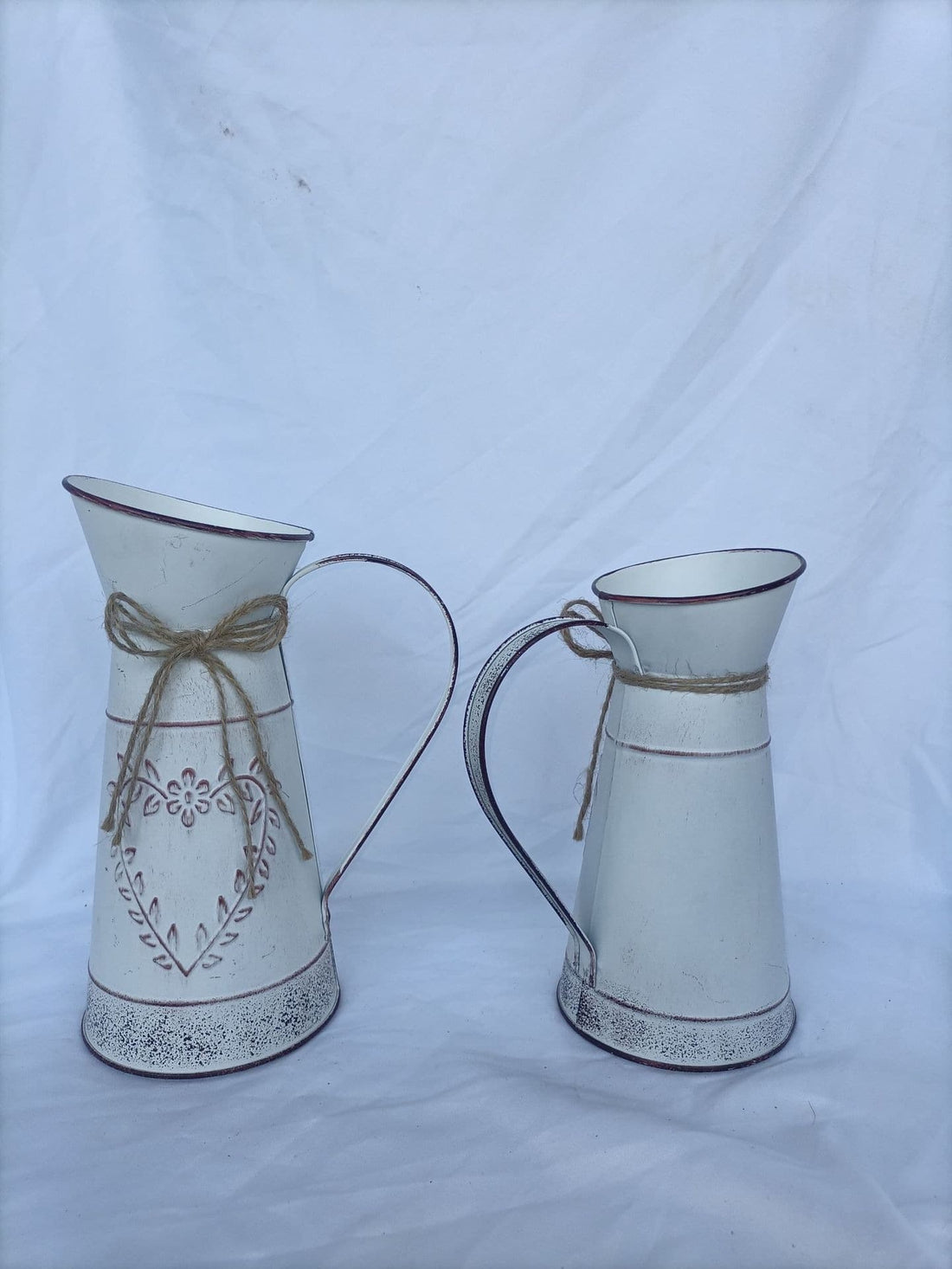 Two distressed metal pitcher vases with embossed floral patterns and jute bows