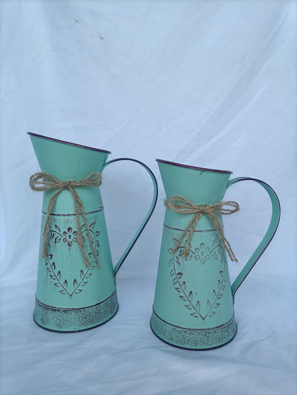 Two turquoise metal jugs with decorative patterns and string bows on a light blue background