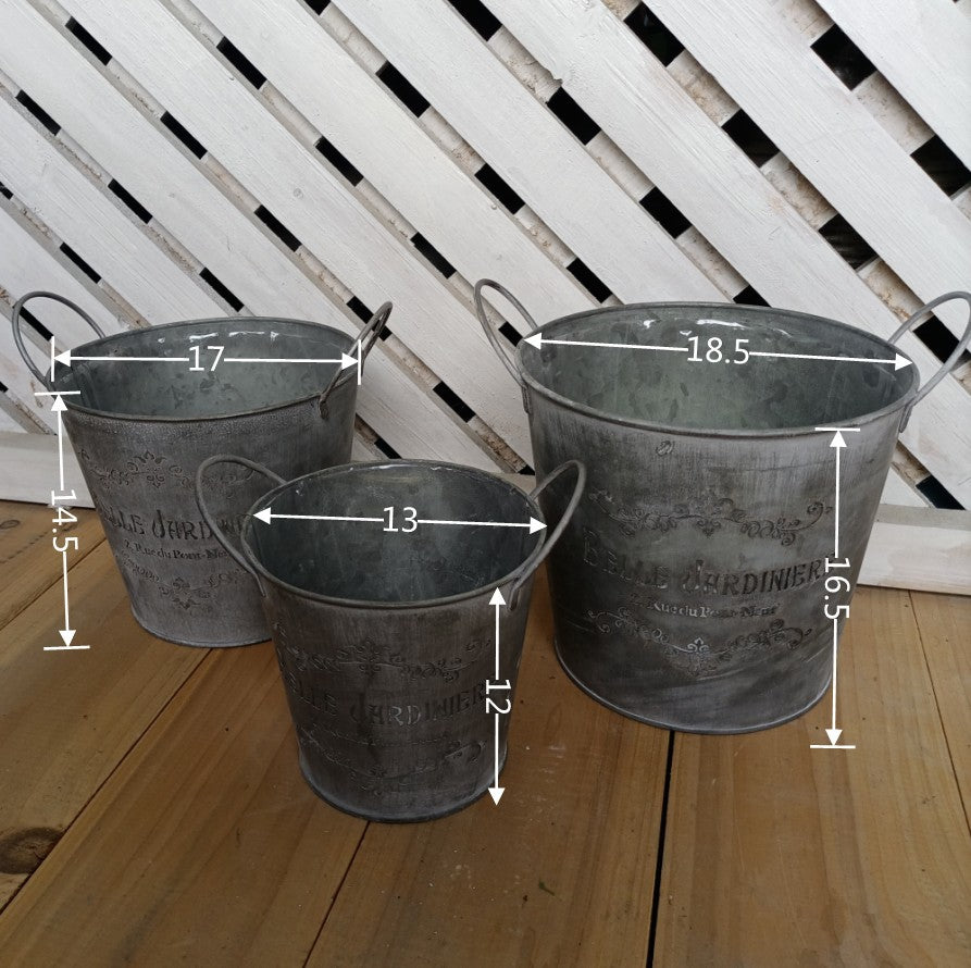 Three metal buckets with dimensions marked on a wooden surface and white lattice background