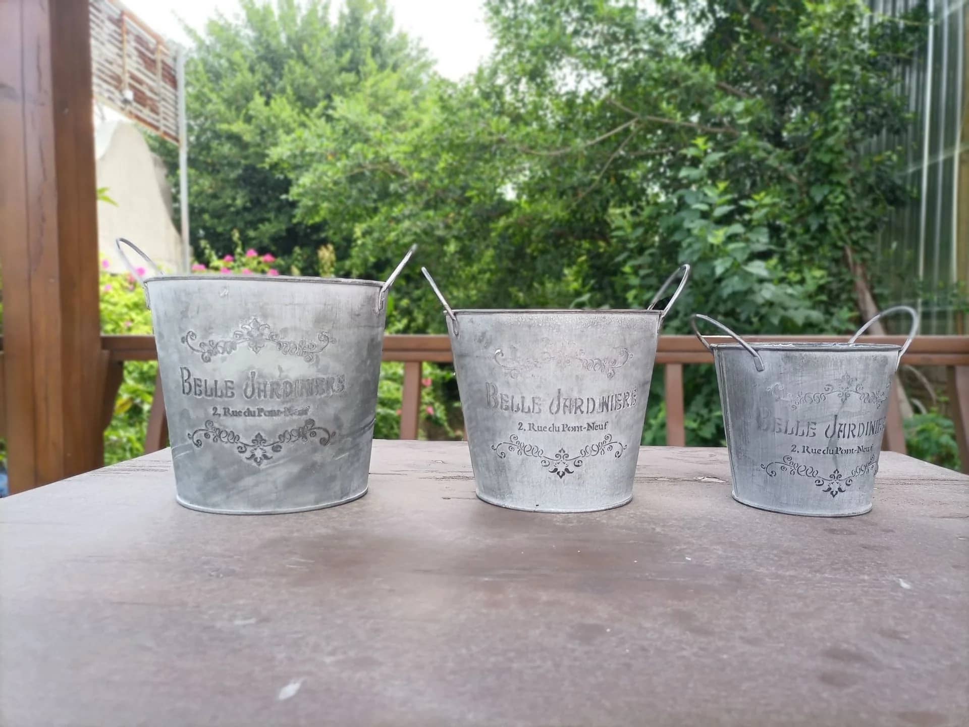 Three metal buckets with engraved text on a wooden surface outdoors.