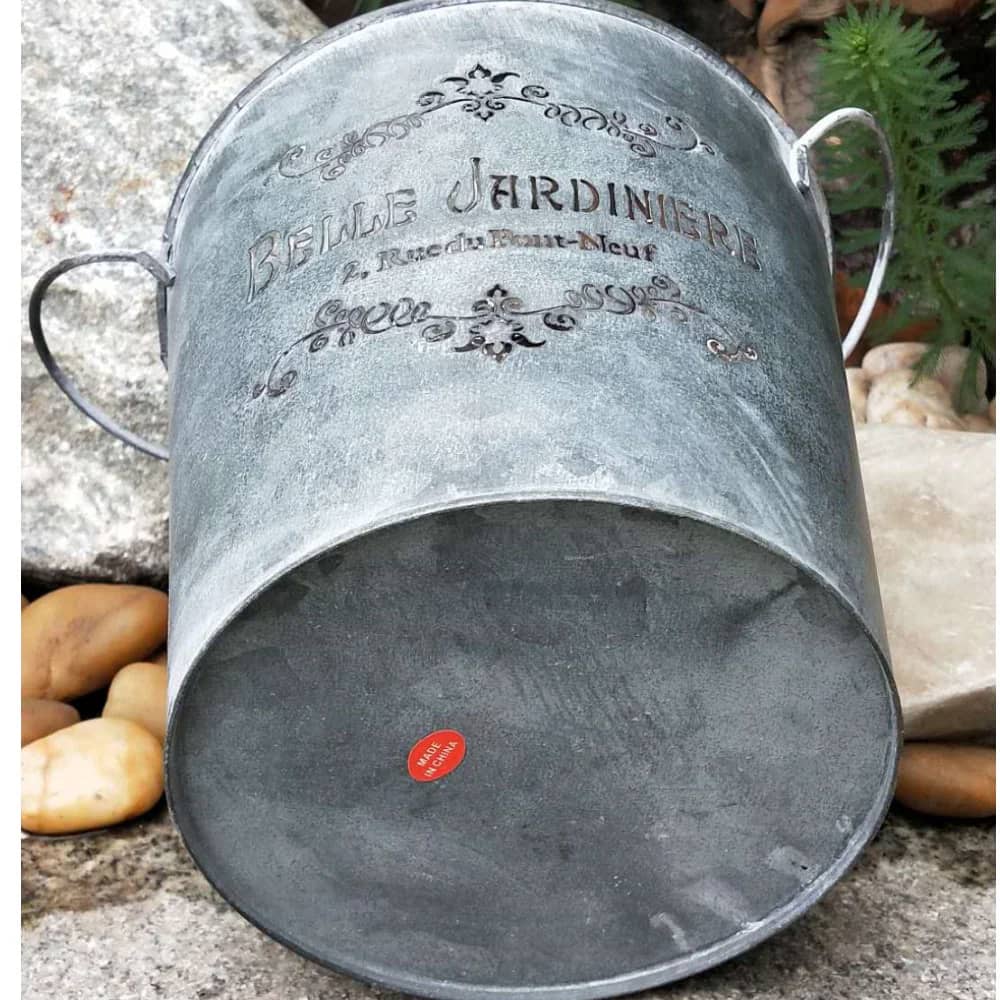 Metal flower pot with decorative text and handles on a stone surface.