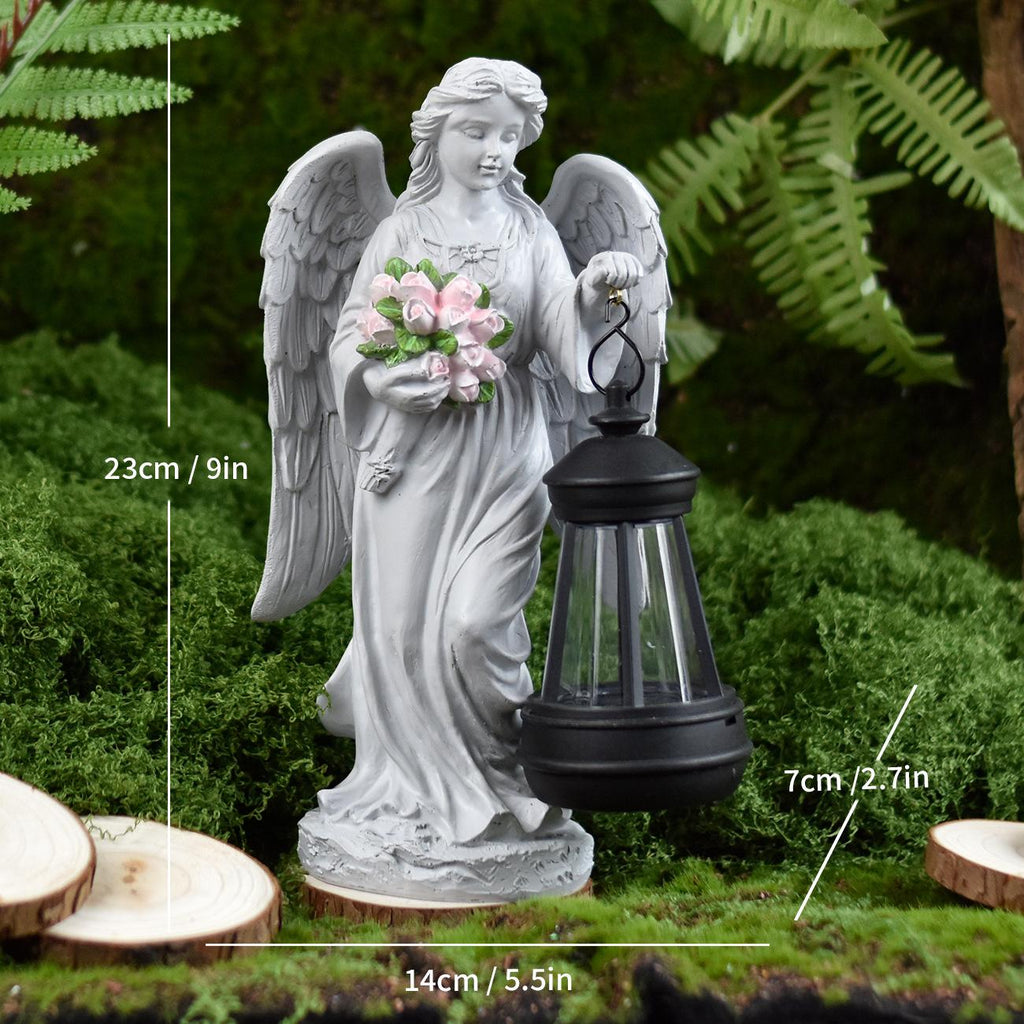 Angel statue with solar lantern and flowers in a garden setting