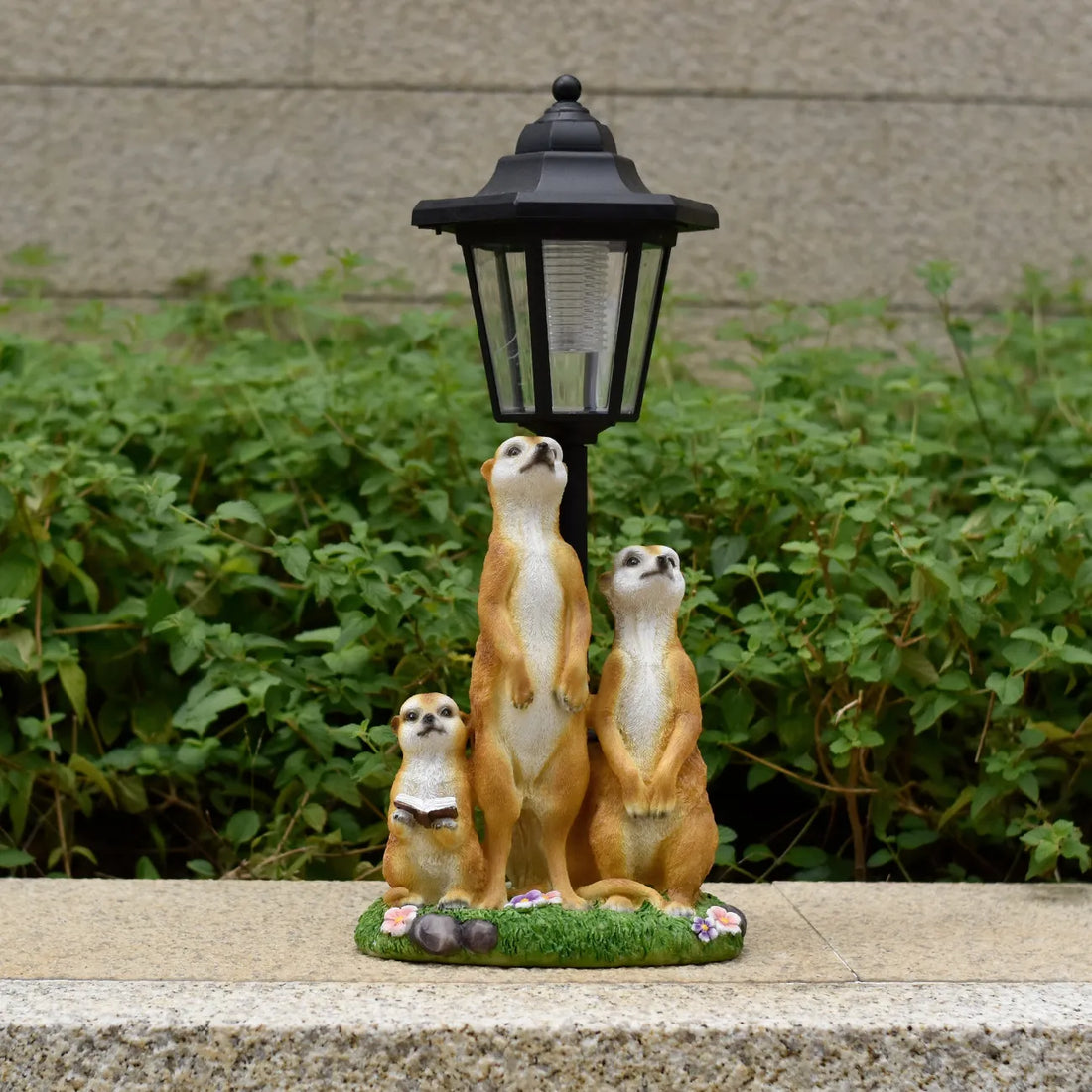 Hand-painted resin meerkat family statue with black LED lantern above, on flower patch.