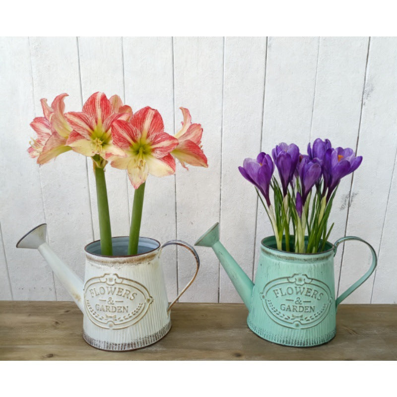 White and teal metal watering can vases with 'Flowers & Garden' emblem, holding colorful blooms.