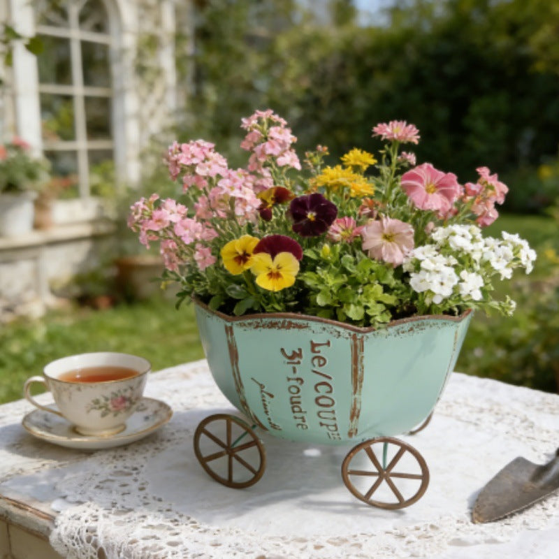 Lyseblå vintage metalplantevogn med hjul og blandede blomster