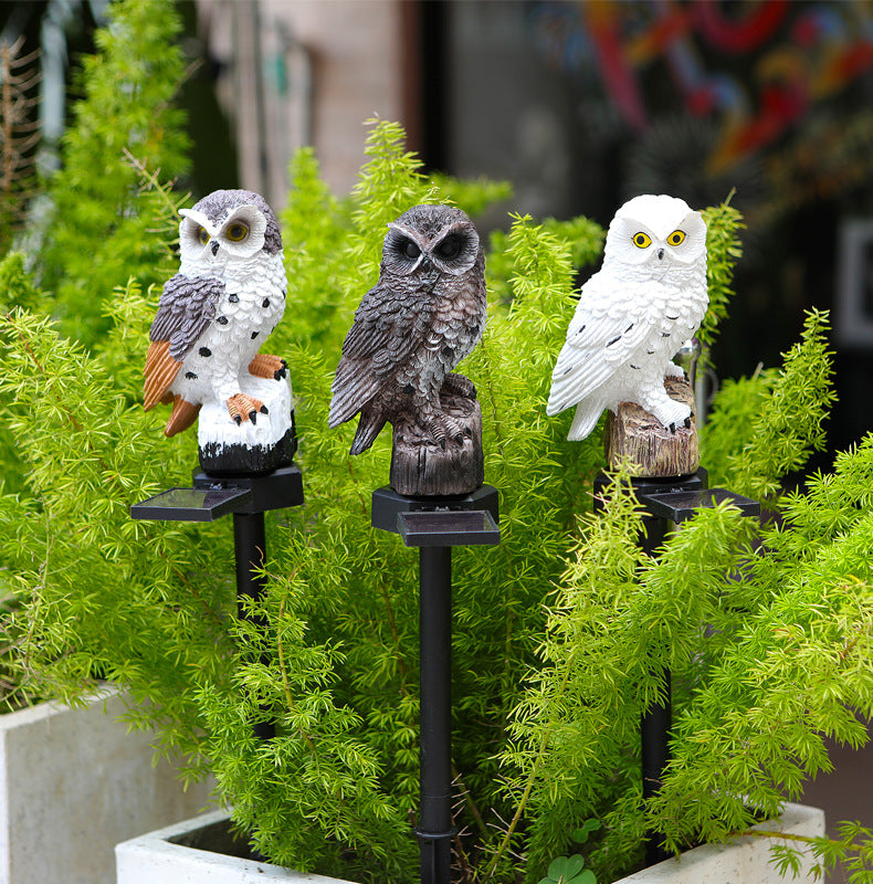 Three owl solar garden stake lights standing in green foliage, glowing bases