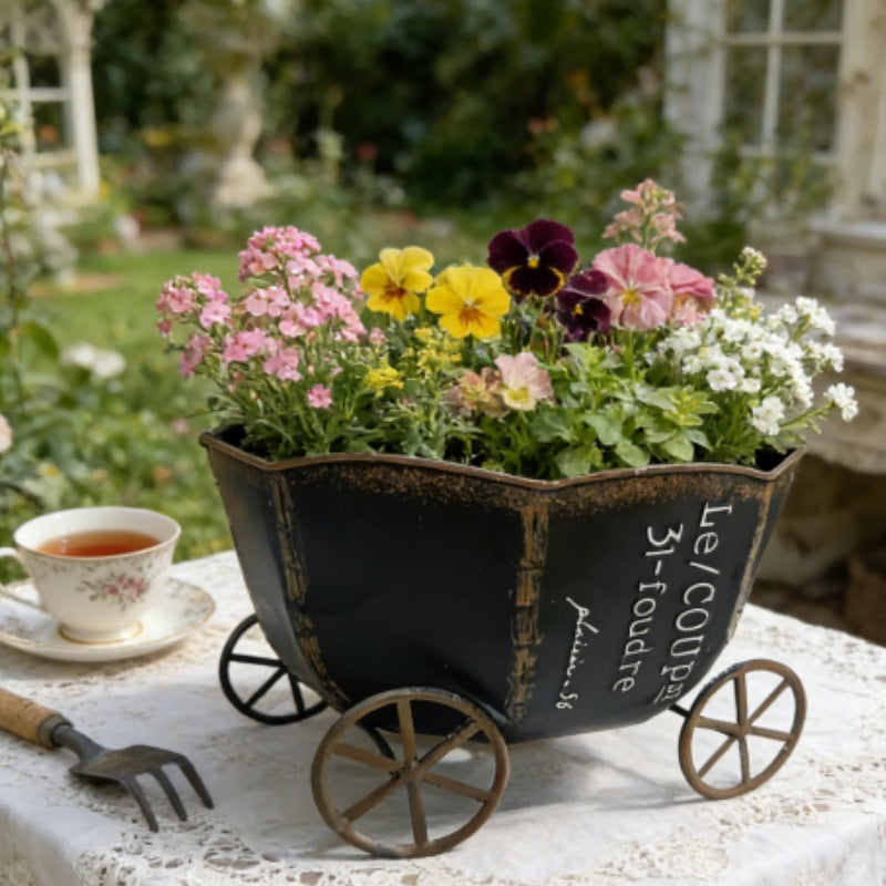 Mørk trækul vintage metalplantevogn med hjul og lyserøde blomster