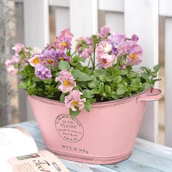 Vintage lyserød oval metalplantekar med sidehåndtag og lilla blomster