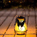 Frosted solar flame lantern glowing on ground, black metal frame with bird silhouette
