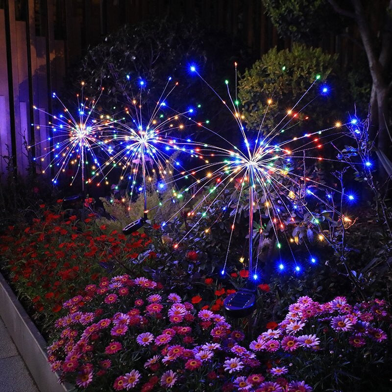 Two LED dandelion solar stake lights glowing multicolor firework bursts