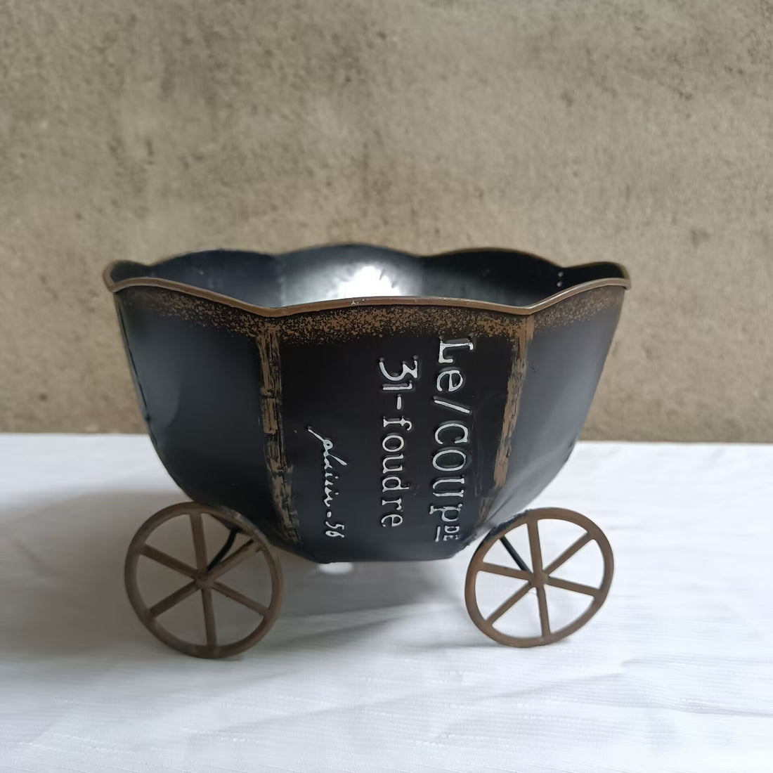 Vintage black metal cart planter with engraved text and decorative four-wheel base
