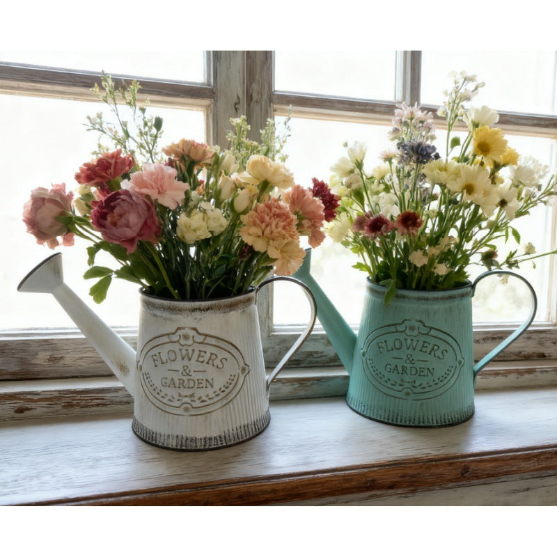 Teal and white metal watering can vases with 'Flowers & Garden' emblem, holding flower bouquets.