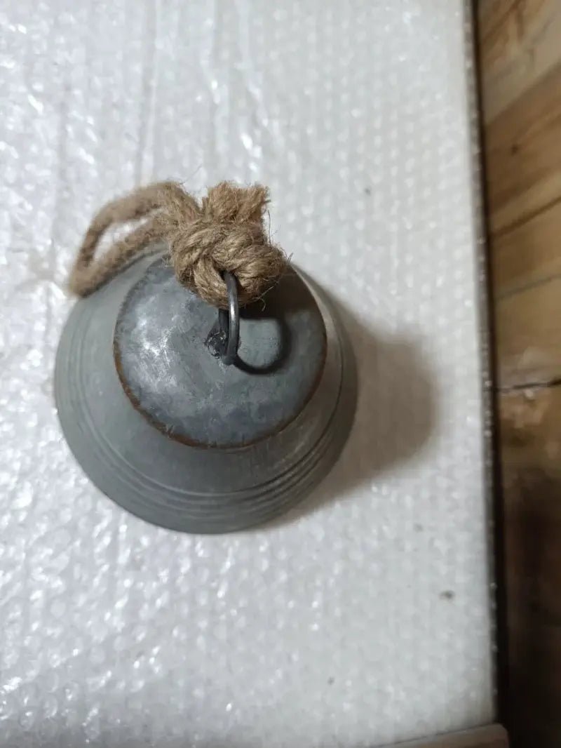 Small weathered gray metal bell with rope loop and wall-mount hook