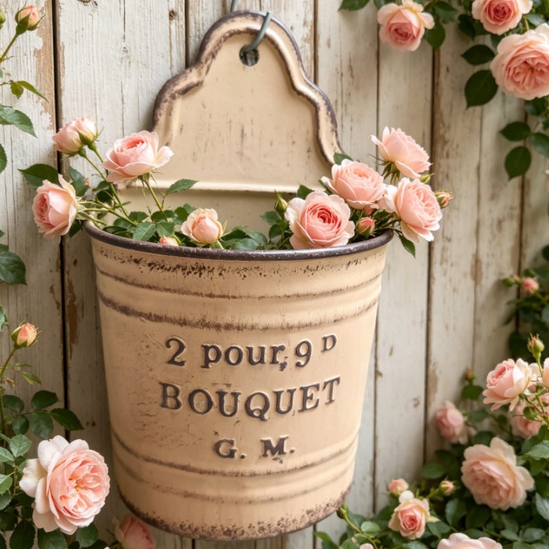 Beige metal wall pocket planter with hanging hook and rose stems inside