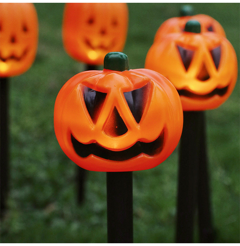 Close-up orange jack-o’-lantern LED garden stake light with carved face on a black post