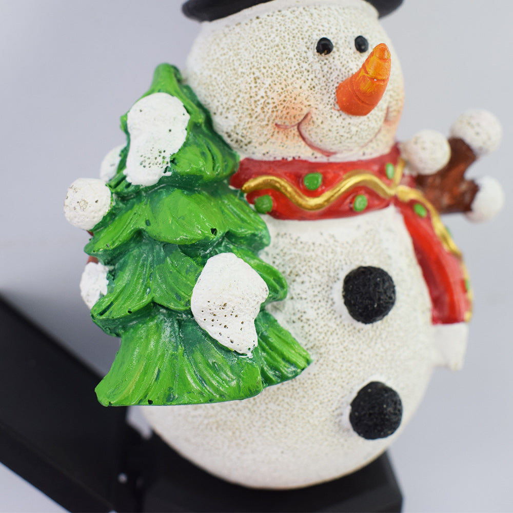 Close-up solar snowman light-up stake holding a green decorated tree.