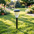 Black solar stake light with clear faceted glass top, glowing over green lawn