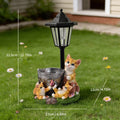 A decorative solar garden light and pet fountain sculpture featuring three orange-and-white cats around a metal bowl with the word 'WELCOME' on a grassy base, shown on a lawn with dimension lines and text indicating height, width, and depth.