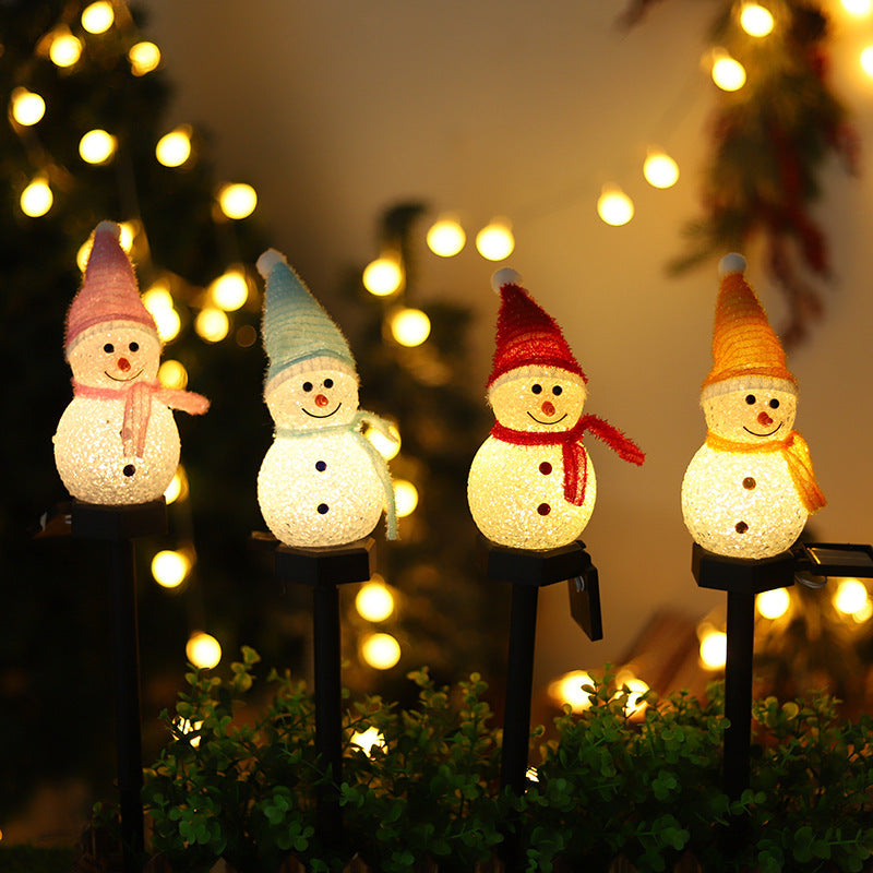 Solar snowman pathway stake lights glowing on bushes with four snowmen and colorful hats