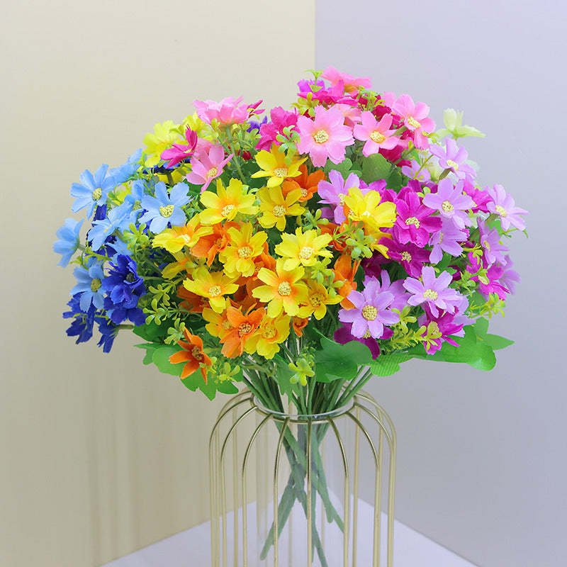 Pink, purple, yellow, and orange faux daisy flower stems in a clear glass vase