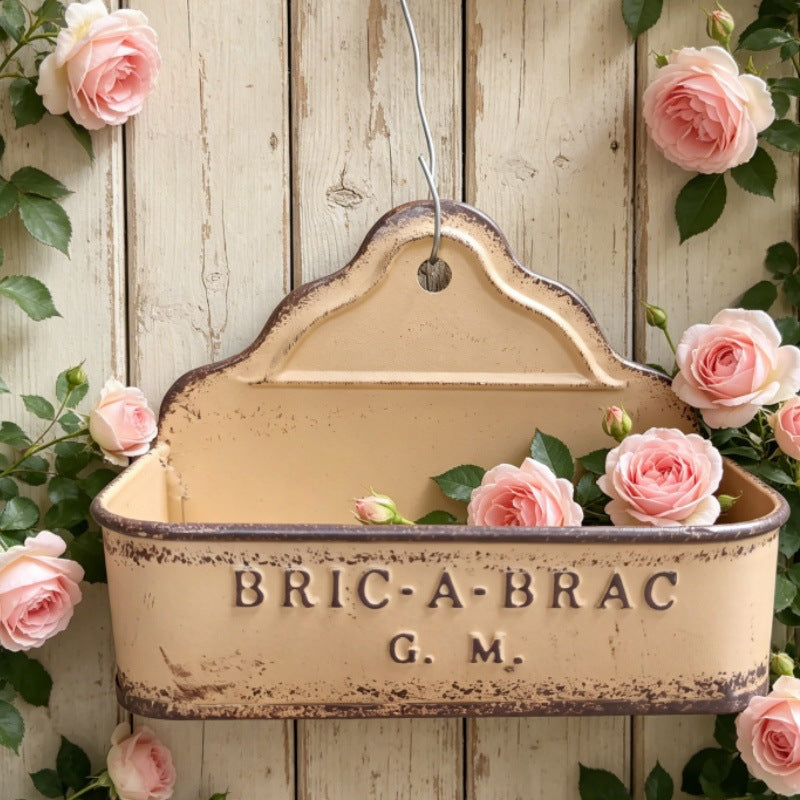 Beige metal wall planter with “BRIC-A-BRAC G.M.” lettering and hanging loop.