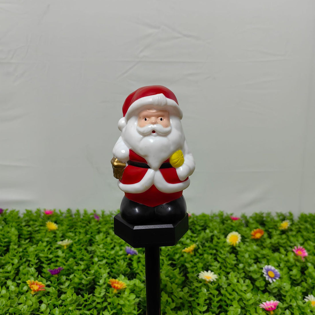 Santa solar stake light on black pole, red coat and white beard holding a gift