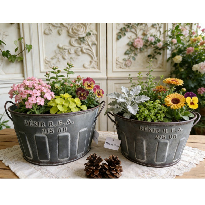 Par mørke, galvaniserede blikpotter med hanke, fyldt med blandede blomster