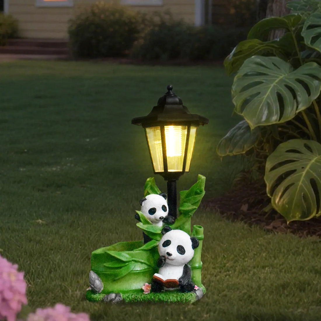 Hand-painted resin panda family garden statue with glowing black LED lantern beside large leaves.