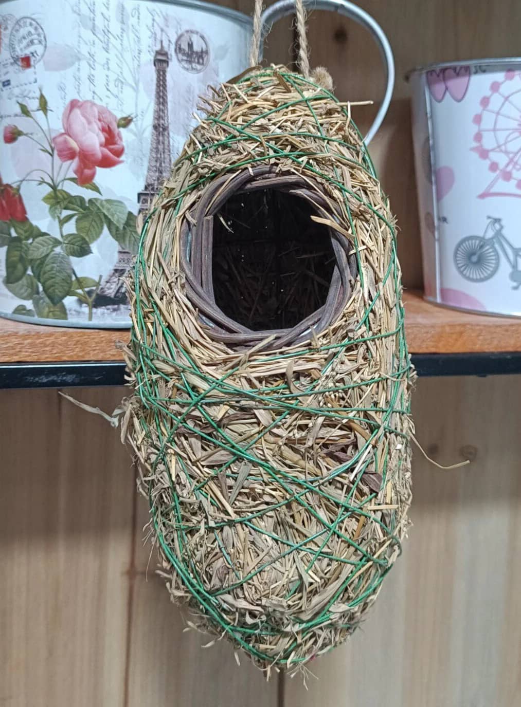 Woven bird nest hanging on a string with decorative tins in the background.