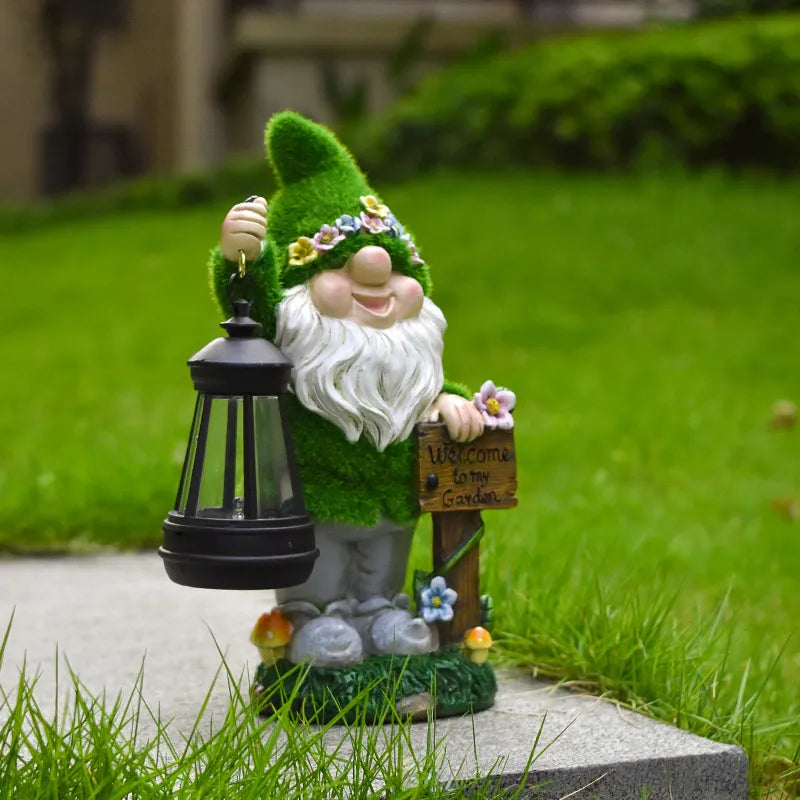 Green-hat resin gnome holding a glowing LED black lantern, flower crown and plaque.