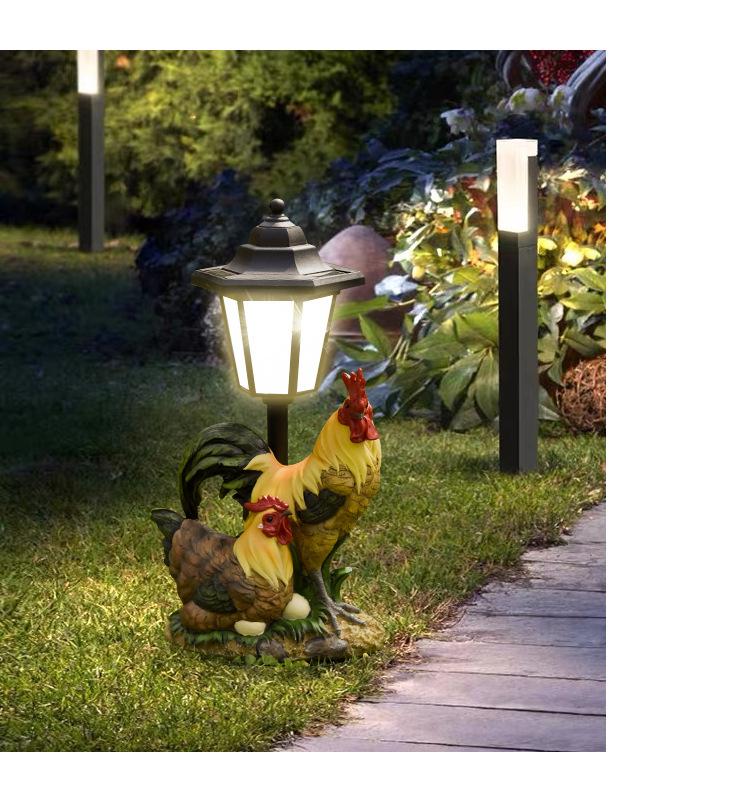 Decorative rooster garden light fixture on a grassy path with a solar lamp in the background.