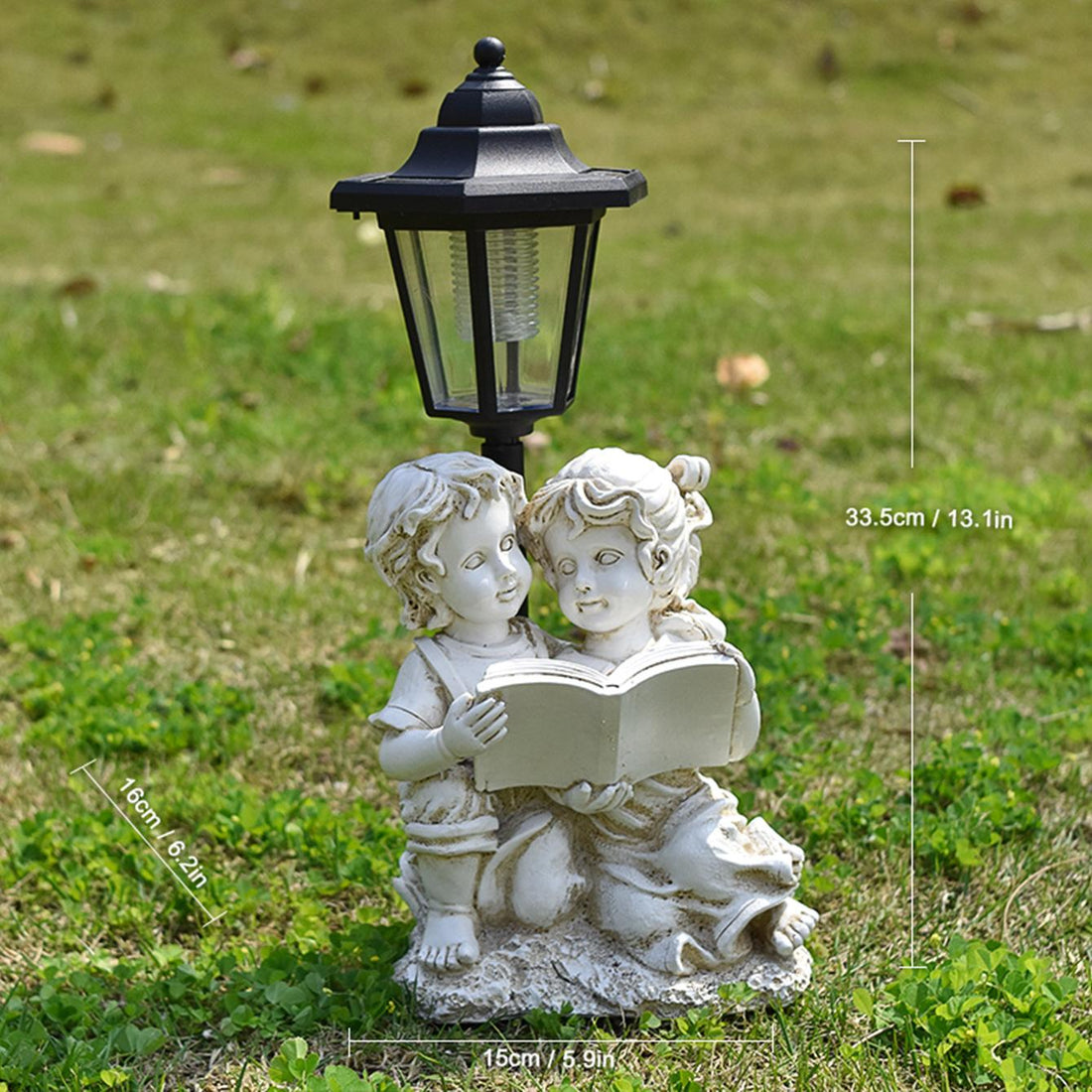 Decorative garden statue of two children with a book and solar lamp on grass