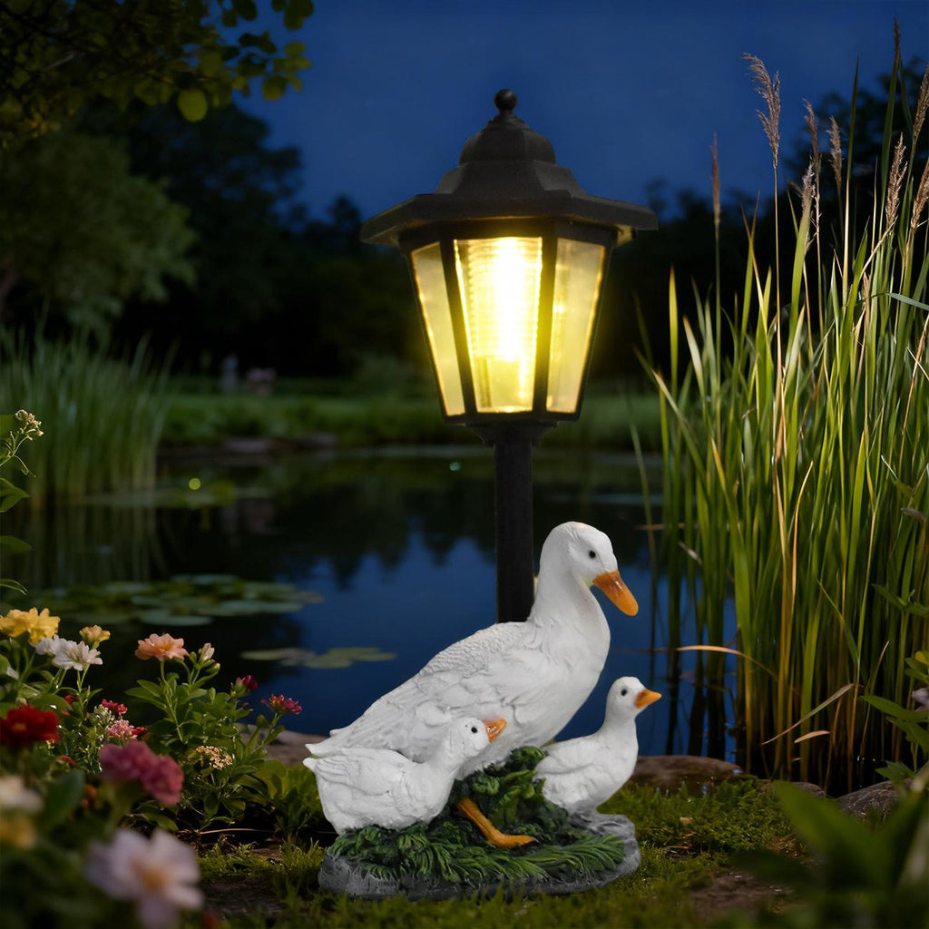 Garden scene with a solar lamp, ducks, and flowers by a pond at night.