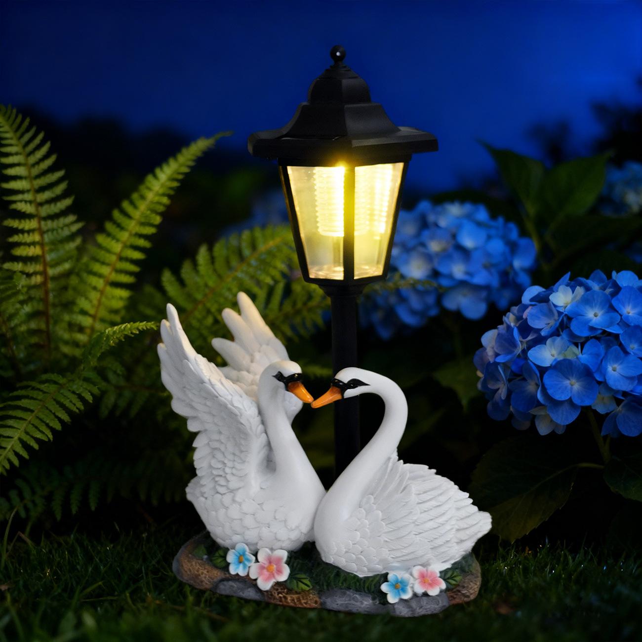 Two swan statues with a solar lamp in a garden setting