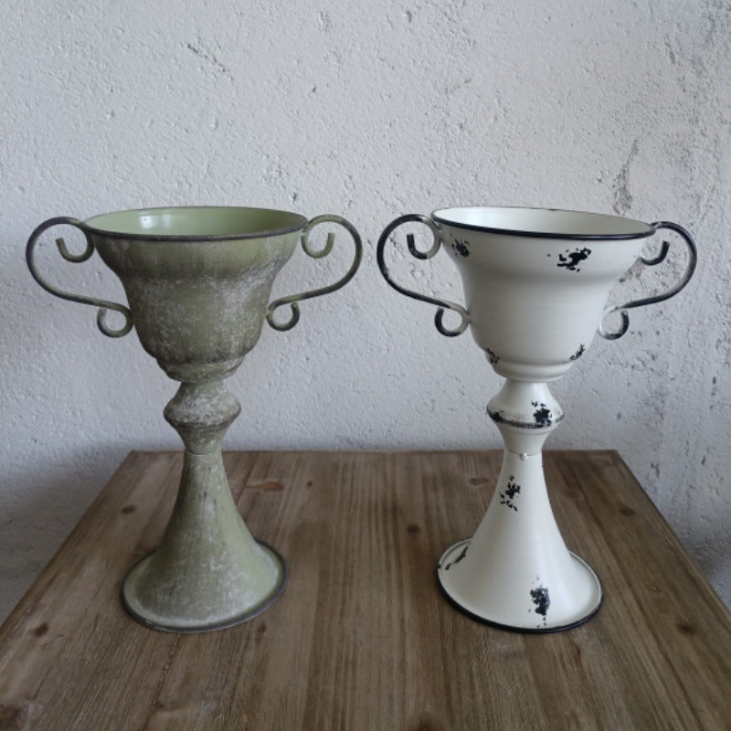 Two decorative urns on a wooden surface with a white textured wall background.