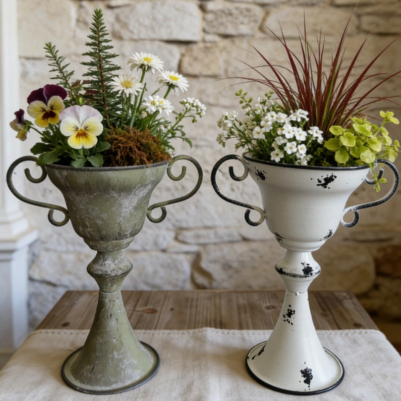 Two decorative planters with flowers on a wooden table against a stone wall.