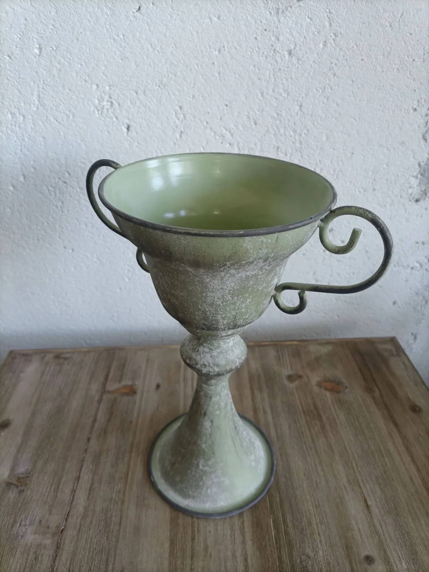 Green ceramic cup with handles on a wooden surface against a white wall