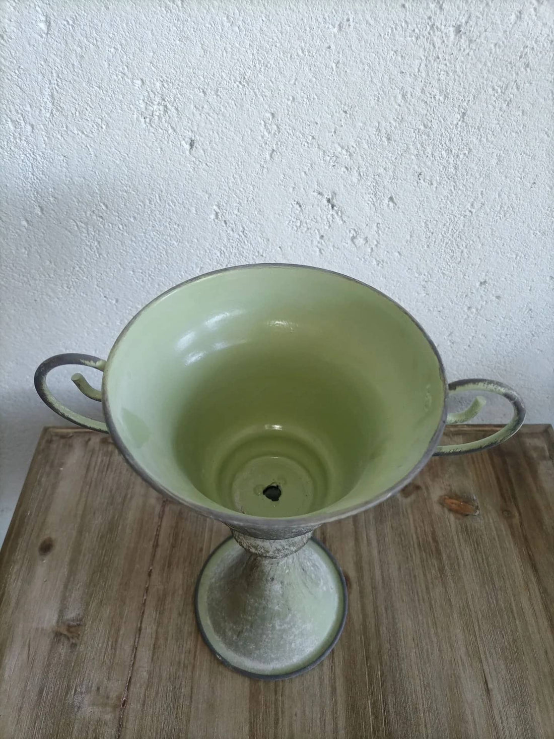 Light green metal planter urn with scrolled handles and central drainage hole on base.