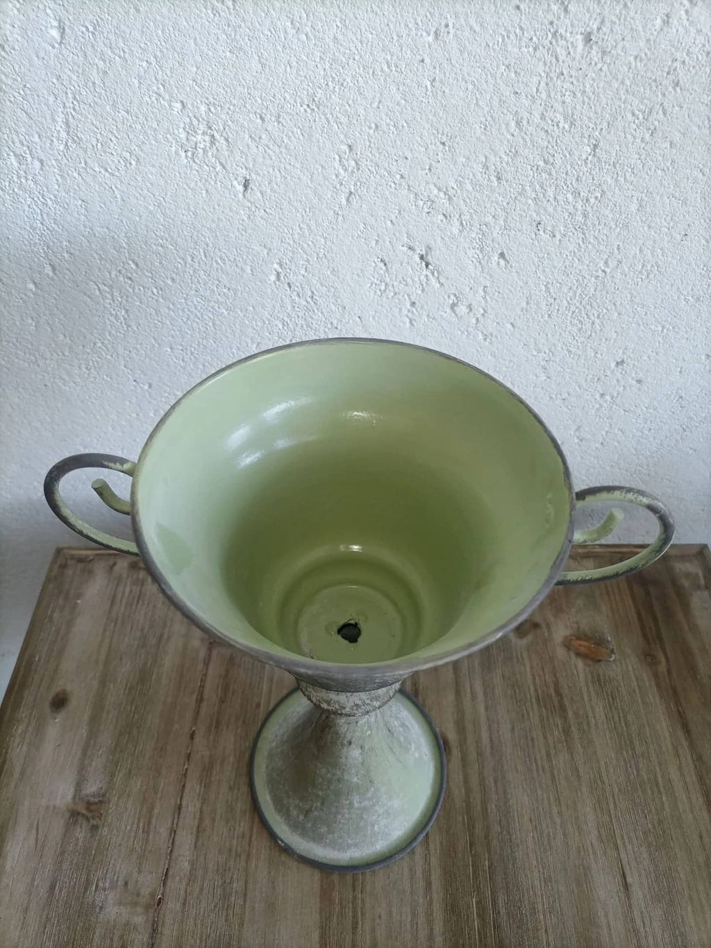 Green ceramic vase with handles on a wooden surface and white wall background
