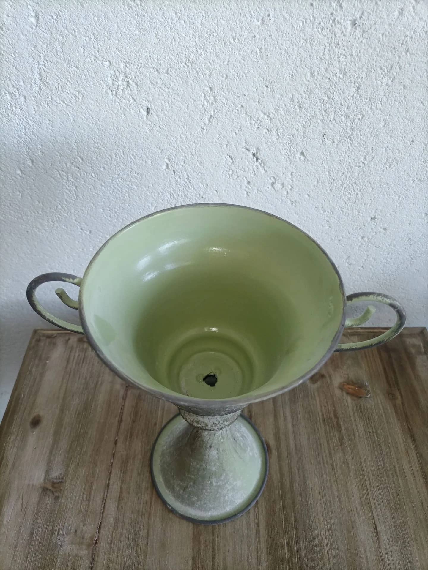 Green ceramic vase with handles on a wooden surface and white wall background